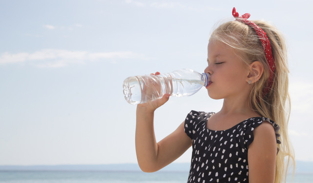 Little girl having water break on the beach to avoid dehydration and heat illness